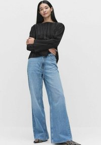 Sort plisseret top med lange ærmer, parret med lyseblå vidde jeans. Sættet har en afslappet pasform og struktureret stof.