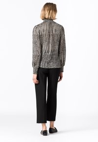 Blusa con motivo bianco e nero, collo alto, maniche lunghe e vestibilità rilassata, abbinata a pantaloni neri a gamba dritta e scarpe flat.