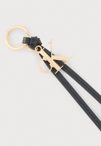 Χρυσό μπρελόκ Calvin Klein με μαύρο δερμάτινο λουράκι και μεγάλο γοητευτικό λογότυπο CK σε απλό ανοιχτό φόντο.