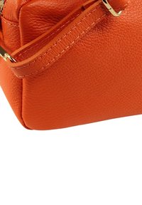 Sac à main en cuir orange à finition texturée, avec des accessoires dorés et une bandoulière plate et large. Design compact et structuré.