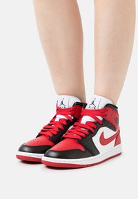 Zapatillas altas que presentan una combinación de colores rojo, negro y blanco. Material de cuero, caja de los dedos perforada, suela blanca gruesa y detalles con logotipos.