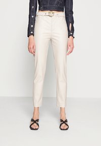 Beiga faux läderbyxor med skräddarsydd passform, med sidofickor och en guldspänne bälte som accent. Styler med svarta remsandaler.