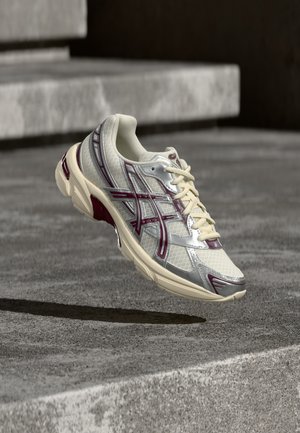 Chaussure de sport blanche et bordeaux en plein air au-dessus d'une surface en béton avec des marches en pierre en arrière-plan.