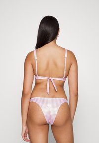 Conjunto de biquíni em padrão gingham cor-de-rosa com alças finas, laço nas costas ajustável e parte inferior de cobertura mínima. Textura suave e acabamento brilhante.