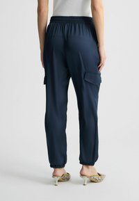 Pantalons de cargo marine avec taille élastique, deux poches latérales et chevilles fendues, associés à des mules à talons imprimé serpent. Texture lisse.