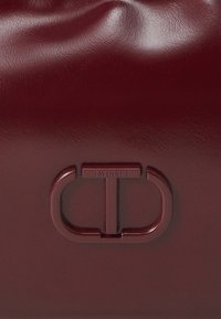 Burgundy leather bag with a glossy finish, featuring a debossed logo in the center and smooth, rounded edges.