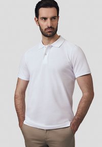 Biała koszulka polo z krótkim rękawem, wykonana z bawełny, z klasycznym kołnierzykiem i zapięciem na trzy guziki. Gładka faktura i dopasowany krój.