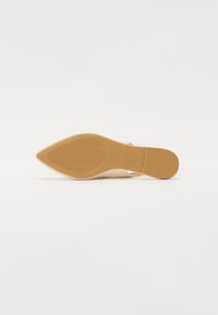 Sandale à talon beige avec un bout pointu et une semelle texturée. Elle présente un matériau supérieur lisse et un talon étroit pour ajouter de la hauteur.