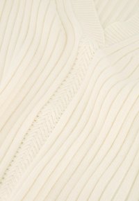 Geribbelde gebreide trui in gebroken wit met verschillende gestructureerde strepen. Heeft een V-halslijn en subtiele zigzag-accenten langs de naden.