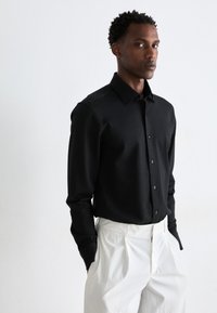 Black long-sleeve shirt with a textured pattern, button-down collar, and front placket, paired with white high-waisted trousers.
