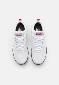 Hvite Skechers Flex-Lite joggesko har et teksturert mesh-overside, flate hvite snørebånd, røde detaljer på hælen og en svart yttersåle.