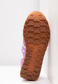 Semelle de chaussure de sport rose et blanche présentant une surface en caoutchouc texturée avec des crampons triangulaires pour la traction et un logo de marque en relief.