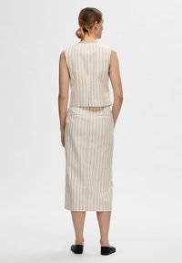 Costum două piese de culoare bej deschis, format dintr-un top scurt fără mâneci și o fustă creion midi cu dungi verticale negre și buzunare laterale.