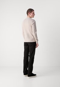 Lys beige genser med lange ermer, ribbet tekstur og rund hals, kombinert med svarte bukser og svarte joggesko, sett fra baksiden.