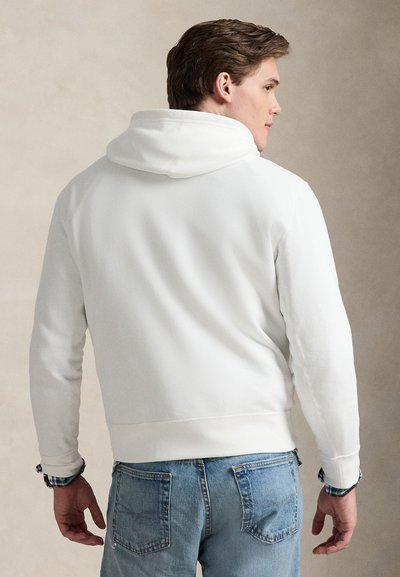 Hvit hettegenser med kængurulomme og snor i hetten, kombinert med lyseblå denimjeans. Stoffet virker mykt med et enkelt design.