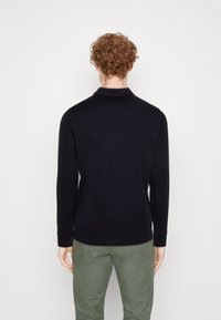 Navy long-sleeve polo shirt with a classic collar, made of soft fabric, featuring a straight hem and ribbed cuffs, worn with olive green pants.