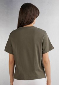 Olivgrön bomulls-t-shirt med korta ärmar och rundad halsringning, med sidoflikar och en avslappnad passform. Slät textur och enkel design.