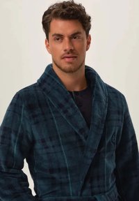 Szlafrok o teksturze wafla w kolorze granatowym, z kołnierzem szalowym, długimi rękawami oraz wzorem w kratę w ciemnych i jasnych odcieniach niebieskiego.