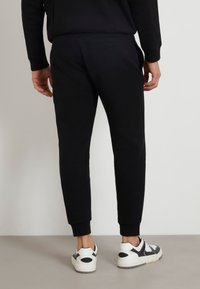 Zwarte joggers met een slim fit, elastische boorden en zijzakken, gecombineerd met zwart-witte sneakers, tegen een neutrale achtergrond.