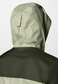 Kurtka z kapturem w jasnobeżowym kapturze i ciemnozielonym górnym panelu pleców, prezentowana z tyłu na jednolitym tle.