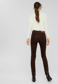 Pantalon en velours côtelé marron taille haute avec une coupe ajustée, doté de poches arrière et d'un tissu texturé. Associé à des bottines noires à talons.