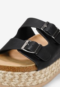 Sandales noires avec deux lanières réglables et boucles en argent. La semelle compensée associe du liège et de la jute tressée pour une texture supplémentaire.