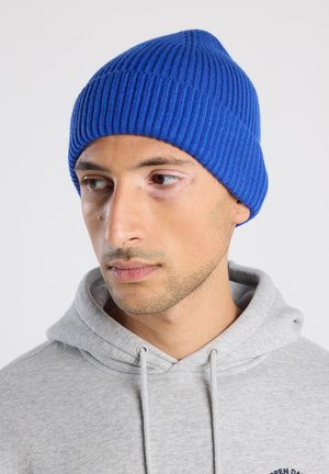 Blauwe geribbelde gebreide beanie met een snug fit, gemaakt van zacht materiaal. Draagt een grijze hoodie met een voorzak en koord.