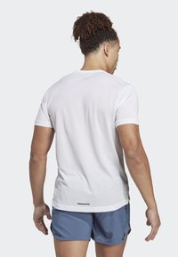Camisa atlética blanca de manga corta con un patrón de malla texturizada, que presenta un escote redondeado y un corte ajustado, combinada con pantalones cortos azules.