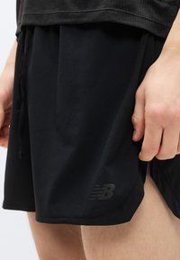 Μαύρα αθλητικά σορτς από ελαφρύ ύφασμα, με κορδόνι για ρύθμιση και μικρό μαύρο λογότυπο στο τελείωμα.