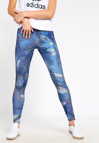Blå leggings med virvlande vita mönster, tillverkade av stretchy material, med en märkeslogo på den övre delen av benet och en figurnära design.