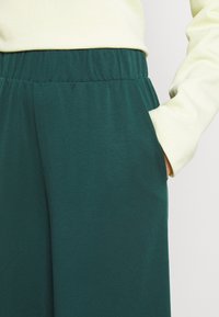 Teal jogger pants made from soft fabric with an elastic waistband and side pockets, paired with a light yellow long-sleeve top.