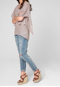 Top a tinta rosa chiaro, con motivo e maniche corte e fluttuanti, abbinato a jeans blu strappati e sandali con zeppa marroni, caratterizzati da una texture intrecciata.