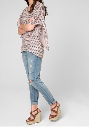 Lys rosa, mønstret top med korte, lette ærmer parret med slidte blå jeans og brune kile-sandaler med vævet tekstur.