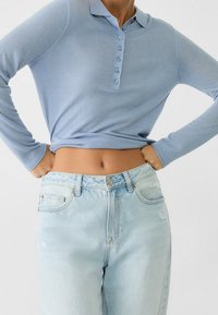 Himmelblaues Langarm-Polohemd mit Kragen und sechs Knöpfen, kombiniert mit hellblauen, leicht abgetragenen High-Waist-Jeans.