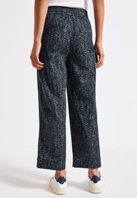 Pantaloni palazzo in un motivo testurizzato nero e teal, con fascia elastica in vita e tasche posteriori, abbinati a sneakers bianche.