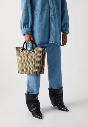 Sac fourre-tout tissé avec un motif noir et fauve, doté de deux poignées et d'une bordure noire. Porté avec un jean bleu clair et des bottes noires à bout pointu.