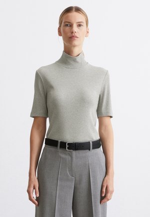 Hellgrau kurzärmeliger Rollkragenpullover mit geripptem Muster, kombiniert mit hochgeschnittenen grauen plissierten Hosen und einem schwarzen Gürtel.