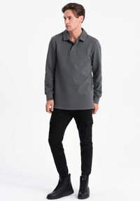 Grijze polo met lange mouwen en kraag, gecombineerd met zwarte cargo-broeken met zijzakken en zwarte hoge laarzen.