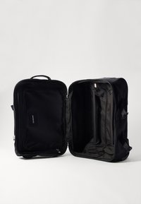 Black soft-sided travel bag with dual zippers, a front pocket, and textured fabric. The interior features compartments and a dark lining.