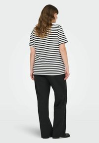 Stribebekledd svart og hvit t-skjorte med løs passform, parret med svarte bukser. Modellen vises fra baksiden, med korte ermer og rund hals.