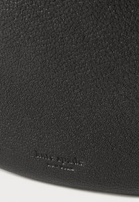 Μαύρη τσάντα από δέρμα με υφή, με χοντρό σπόρο και ανάγλυφο λογότυπο της μάρκας κοντά στον πάτο. Απλός, μινιμαλιστικός σχεδιασμός.