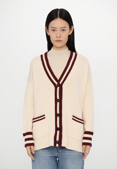 Cream cardigan with a deep V-neck, burgundy striped accents, black buttons, and side pockets. Knit texture, relaxed fit, and long sleeves.