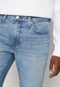 Lyseblå denimjeans med en tettsittende design, med kobberfarget beslag, oransje sømmer og frontlommer. Midjebånd med knappelukking.