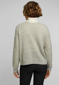Ljusgrå tröja med en texturerad yta, med en kortad design och kabelstickade detaljer på de långa ärmarna.