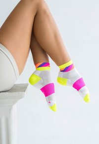 Bunte Sportsocken mit weißem Grund und neonpink, gelben und lila geometrischen Mustern; Knöchelhöhe mit strukturierten Abschnitten.