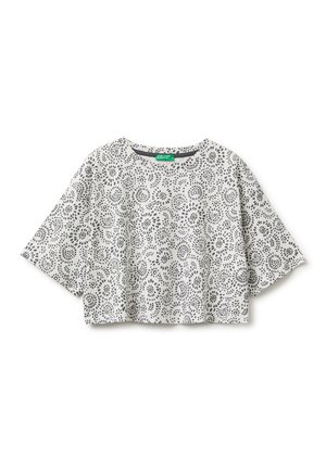 Crop top blanc à manches courtes avec des motifs circulaires noirs en pointillés répartis uniformément sur le tissu, présenté sur un fond blanc uni.