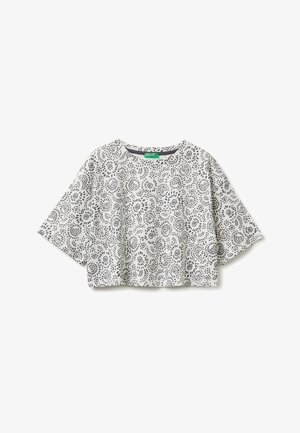 Biały krótki crop top z czarnymi kropkowanymi okrągłymi wzorami równomiernie rozłożonymi na tkaninie, pokazany na płaskim białym tle.