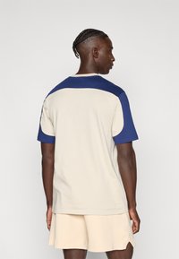 Majica s kratkimi rokavi v kremni barvi z modrimi poudarki, okrogel izrez in sproščen kroj, narejena iz mehkega bombažnega materiala.