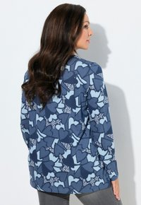 Blauw shirt met lange mouwen met een hartjespatroon in verschillende tinten blauw en witte accenten. De stof oogt glad en heeft een ontspannen pasvorm.