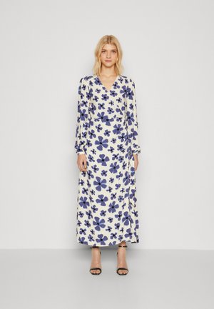 Long-sleeve, V-neck dress in cream with dark blue floral print. Lightweight fabric, fitted bodice, and flowing skirt. Accented with a tie detail.